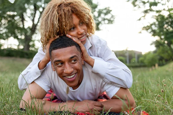 アフリカ系アメリカ人の若い恋人たちが夏に公園の草の上に横になり笑顔で彼女のボーイフレンドの背中に横たわって喜び — ストック写真