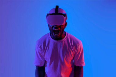 Şok olmuş Afrikalı Amerikalı adam sanal gerçeklik gözlüğü takıyor neon ışıkta çığlık atıyor, korkmuş adam stres altında VR gözlük kullanıyor.