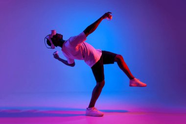 Sanal gerçeklik gözlüklü Afro-Amerikan adam joystickleri tutuyor ve neon ışıkta sıyrılıyor, oyuncu gözlük kullanıyor ve kontrol panellerini tutuyor.