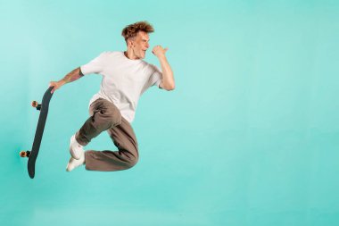 Genç çılgın adam kaykaya biniyor ve mavi izole arka planda zıplıyor, güneş gözlüklü hippi havada kaykayla uçuyor ve ekstrem numaralar yapıyor ve reklamlar alanı kopyalıyor.