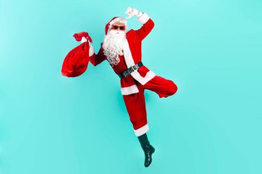Bir çanta dolusu hediyeyle Noel Baba atlıyor ve mavi izole edilmiş arka planda hızla havada uçuyor. Noel Baba uçuyor ve yeni yıl için acele ediyor.