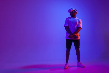 Afro-Amerikan adam sanal gerçeklik gözlükleriyle video oyunu oynuyor, neon ışıklı, modern VR aygıtı kullanıyor ve fotokopi uzayına bakıyor.