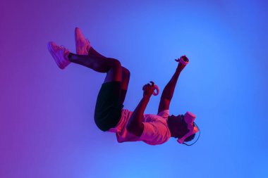 Sanal gerçeklik gözlüklü Afro-Amerikan bir adam havada süzülüyor ve neon ışıklarıyla havaya düşüyor, adam VR gözlükleriyle uçuyor, fantezi ve hayal gücü kavramı