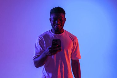Afro-Amerikan adam akıllı telefon kullanıyor ve neon ışıkla gülümsüyor, adam internette yazı yazıyor ve cep telefonuna bakıyor.
