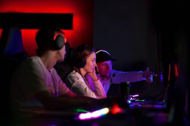 Genç bilgisayar ekibi birlikte stratejiyi tartışıyor ve bilgisayar monitörüne bakıyor, oyuncular bilgisayar kulübünde iletişim kuruyor.