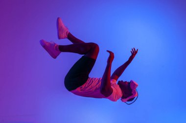 Sanal gerçeklik gözlüklü Afro-Amerikan bir adam havada uçuyor ve neon ışıkta hayali bir şeye dokunuyor, adam düşüyor ve VR gözlükleriyle havada uçuyor ve parmağını gösteriyor.