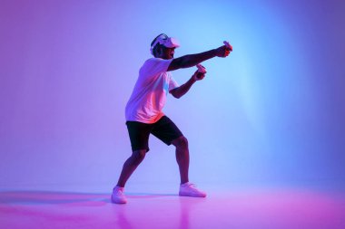 Sanal gerçeklik gözlüklü Afro-Amerikan bir adam, neon ışıkta nişan alıyor ve ateş ediyor, oyuncu oyun oynuyor ve joysticklerle VR gözlükleriyle dövüşüyor.