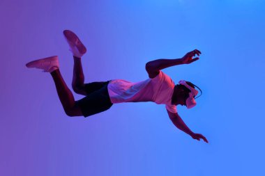 Sanal gerçeklik gözlüklü Afro-Amerikan adam düşer ve neon ışıkta uçar, oyuncu VR gözlük kullanır ve yüzmeyi hayal eder.