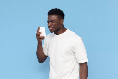 Beyaz tişörtlü Afrikalı genç adam mavi arka planda peçeteye hapşırıyor, adam soğuk algınlığı belirtileri gösteriyor, grip ve reklam alanı kopyalıyor.