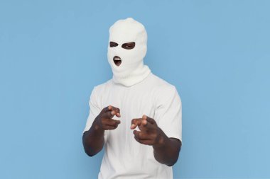 Seni seçiyorum. Beyaz kar maskeli Afro-Amerikan erkek zorba, mavi izole edilmiş arka planda ellerini kameraya uzatarak tehdit ediyor. Maskeli adam çığlık atıyor.