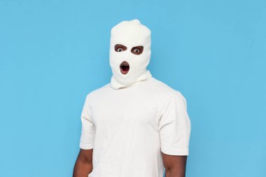 Beyaz kar maskeli afro-amerikan erkek haydut, mavi izole arka planda, ağzı açık, maskeli, tanınmamış bir holigan görünce şaşırır.