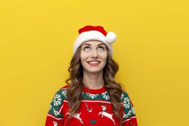 Noel süveteri ve Noel Baba şapkalı genç kız gülümser ve sarı izole edilmiş arka plandaki fotokopi alanına bakar. Noel elbiseli kadın yukarıdan boş boşluğa bakar.