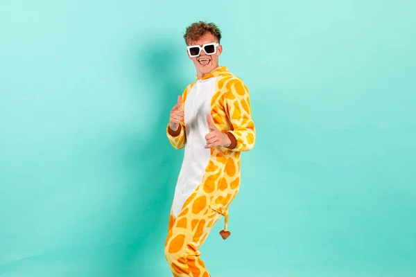 I choose you. young funny guy in orange giraffe pajamas dances at party in sunglasses and points at you on blue isolated background, man in animal costume shows to the camera with his hands