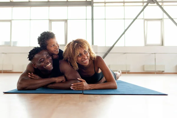 african american young happy family in sportswear lies on a yoga mat in the gym and rests, father mom and son on fitness training relax together and look at copy space