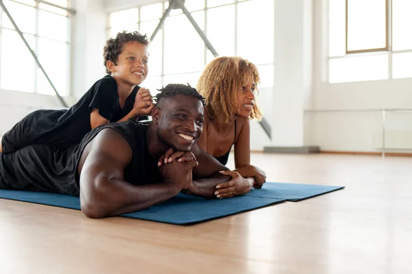african american young happy family in sportswear lies on a yoga mat in the gym and rests, father mom and son on fitness training relax together and look at copy space