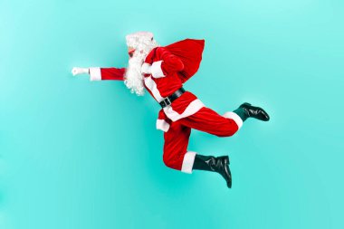 Bir çanta dolusu hediyeyle Noel Baba atlıyor ve mavi izole edilmiş arka planda hızla havada uçuyor. Noel Baba uçuyor ve yeni yıl için acele ediyor.