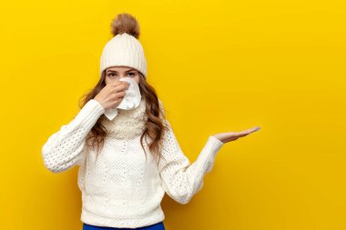 Sıcak, yumuşak kış kıyafetleri içinde, peçeteli, sarı izole edilmiş arka planda soğuk bir kadın, rahat ve rahat örülmüş kazaklı soğuk bir kadın grip ve soğuk algınlığı belirtileri gösteriyor.