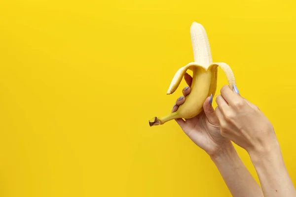 girl\'s hands peel and open banana on yellow isolated background, close-up of the fruit in the hands