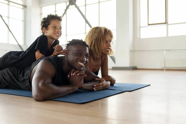 athletic african american young family lies and rests on yoga mat in the gym, mom dad and son go in for sports together, boy of 9 years old with his parents do yoga and look at copy space