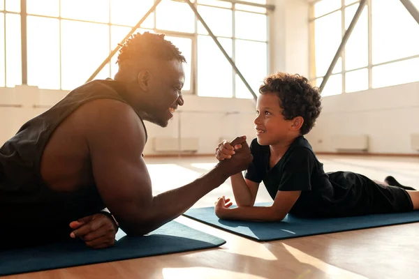 african american boy 9 years old competes with dad in arm wrestling, father trains his son and tests his strength, the concept of education and healthy lifestyle