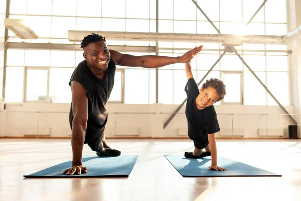 father and son do sports in the gym and give high five, african american boy with dad do push ups from the floor on yoga mat and show success gesture