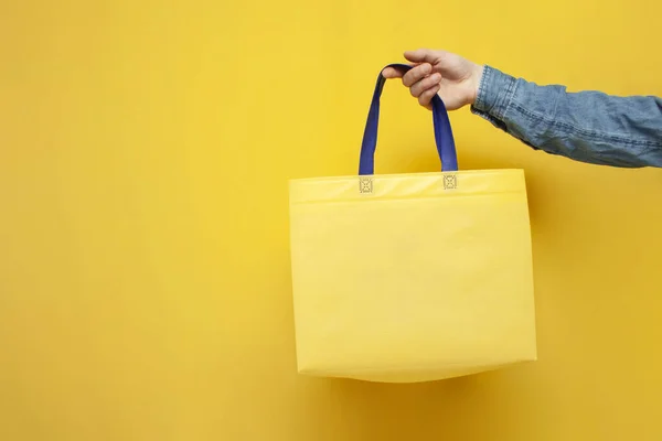 empty fabric eco bag on a yellow background, the guy\'s hand holds a reusable non-plastic bag, the concept of rejecting plastic and ecology