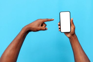 Afro-Amerikan erkek elleri mavi izole edilmiş arka planda boş akıllı telefon ekranı gösteriyor, eller reklam yapıyor ve telefondaki kopyalama alanını gösteriyor.