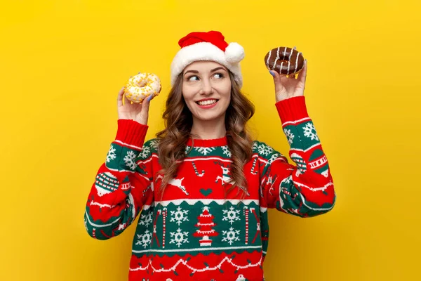 Девушка Рождественском Свитере Шляпе Санта Клауса Держит Два Пончика Думает — стоковое фото