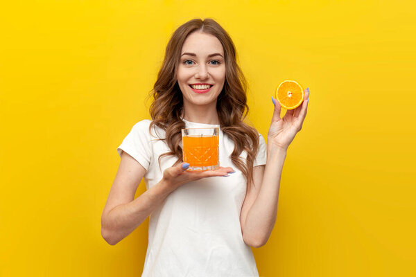 young cute girl with orange drinks orange juice from glass on yellow isolated background, woman with drink and citrus fruit