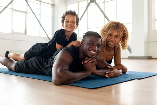 athletic african american young family lies and rests on yoga mat in the gym, mom dad and son go in for sports together, boy of 9 years old with his parents do yoga