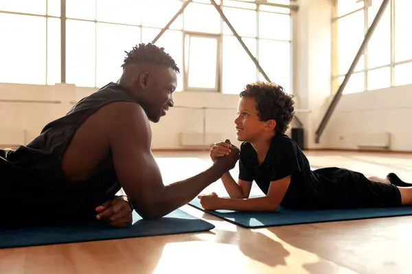 african american boy 9 years old competes with dad in arm wrestling, father trains his son and tests his strength, the concept of education and healthy lifestyle