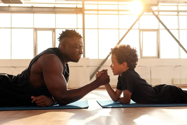 African American man with his son is engaged in arm wrestling in the gym, dad measures his strength with his son and teaches healthy lifestyle