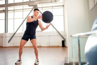 Spor giyimli genç bir adam spor salonunda spor yapıyor. Parlak spor salonunda topla egzersiz yapıyor. Spor ve spor için spor salonuna gidiyor.