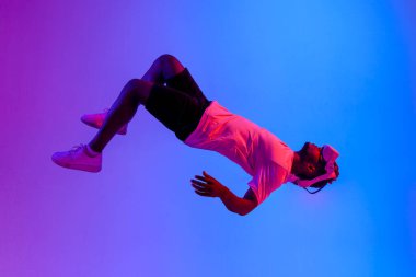 Sanal gerçeklik gözlüklü Afro-Amerikan erkek oyuncu havada uçar ve neon ışığa düşer, adam VR cihazıyla oynar ve havada asılı kalır, hayal gücü ve fantezi kavramı