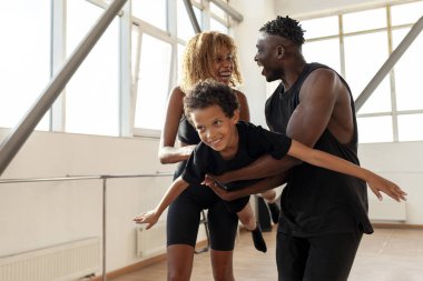 Spor giyim sektöründe Afro-Amerikan ailesi oğlunu havada tutuyor ve taşıyor, spor salonunda oynuyor, ailesinin kollarında çocuk uçuyor ve eğleniyor, özgürlük ve sağlıklı yaşam tarzı kavramı