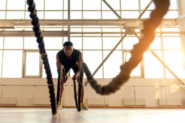 Spor giyinen Afrikalı Amerikalı bir adam spor salonunda sabah antrenman yapıyor, adam halatları sallıyor ve spor salonunda spor yapıyor.