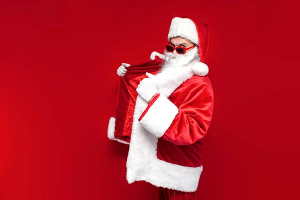 サンタクロース お祝いの眼鏡と赤い背景の帽子のドレス サンタのコスチュームのマニアは暖かい毛皮のコートに置きます — ストック写真