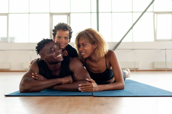 athletic african american young family lies and rests on yoga mat in the gym, mom dad and son go in for sports together, boy of 9 years old with his parents do yoga