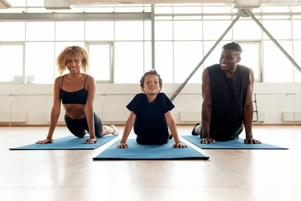African-American family meditates and does yoga on mats, the boy does exercises with his parents in the gym