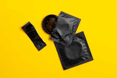torn black pack of a condom lies on a yellow background, the concept of safe sex