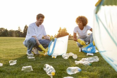 Eldivenli ve çöp torbalarıyla parktaki plastik ve çöpleri kaldıran bir grup çok ırklı insan, gönüllülerden oluşan bir ekip plastik şişeleri toplayıp çalışıyor, insanlar çevreye, yeşil gezegene önem veriyor.