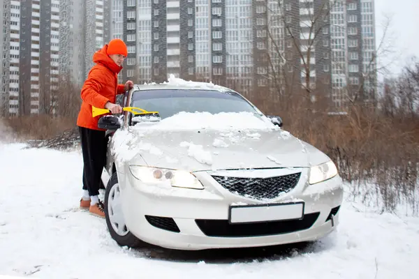 young guy cleans the snow with a brush from the car, a man takes care of the car in winter
