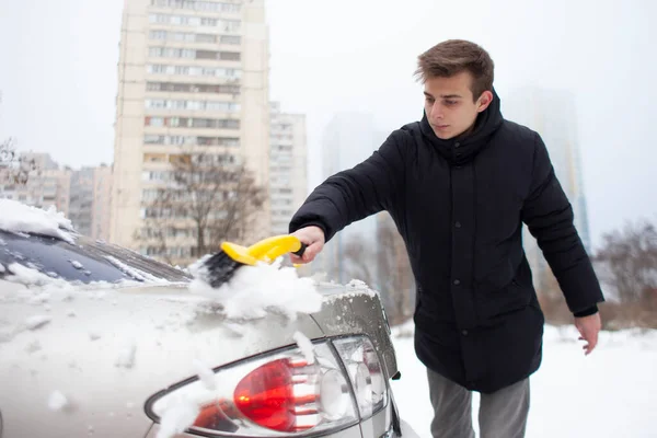 young guy cleans the snow with a brush from the car, a man takes care of the car in winter
