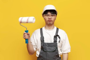 Üniformalı kafası karışmış Asyalı erkek ressam sarı izole edilmiş arka planda sıkılmış. Kafası karışık Koreli inşaat işçisi.
