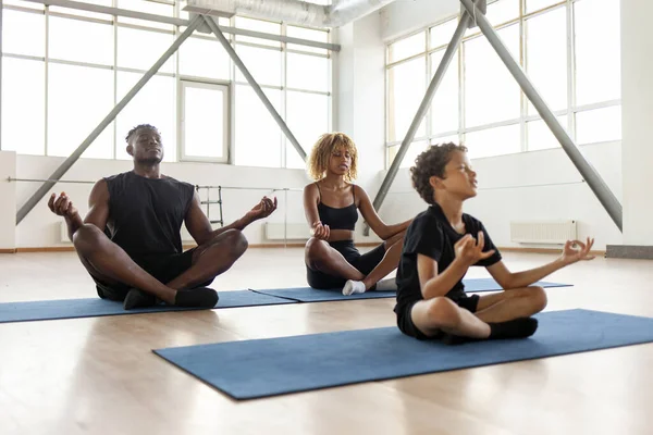 African American family meditates and does yoga on mats, boy sits in lotus position with mom and dad