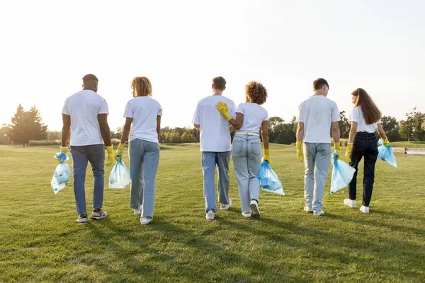 Çöp torbalarıyla eldiven giyen çok ırklı bir grup gönüllü parktan çöp ve plastik topluyor, öğrencilerden oluşan bir grup gezegene yardım ediyor, gençlik çevreyle ilgileniyor, dikiz aynasından bakıyor.