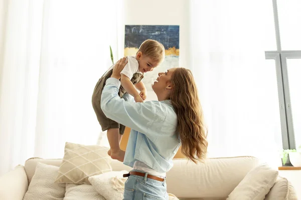 stock image mother plays and rejoices with her little son at home, a young woman lifts her child up and laughs together in the room