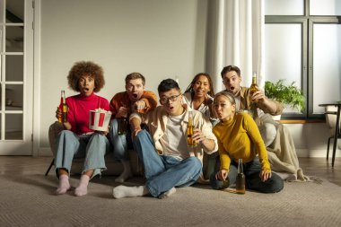 Çok ırklı, şok olmuş bir grup genç arkadaş evlerinde kanepede oturmuş bira içiyor ve şaşkınlıkla televizyon izliyorlar. Şaşırmış öğrenciler alkol içip patlamış mısır yiyor ve kameraya bakıyorlardı.