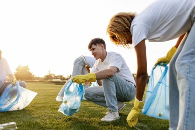 Çöp torbalarıyla çok ırklı bir grup gönüllü parkta çöp ve plastik topluyor, öğrencilerden oluşan bir grup temiz çevre, yeşil gezegen kavramı ve plastik yasağı
