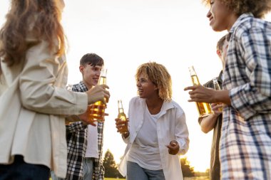 Bir grup çok ırklı genç ellerinde bira şişeleri ve açık hava partisinde konuşuyorlar. Afrikalı Amerikalı kız ve erkek arkadaşları parkta gülüyor ve içki içiyorlar.